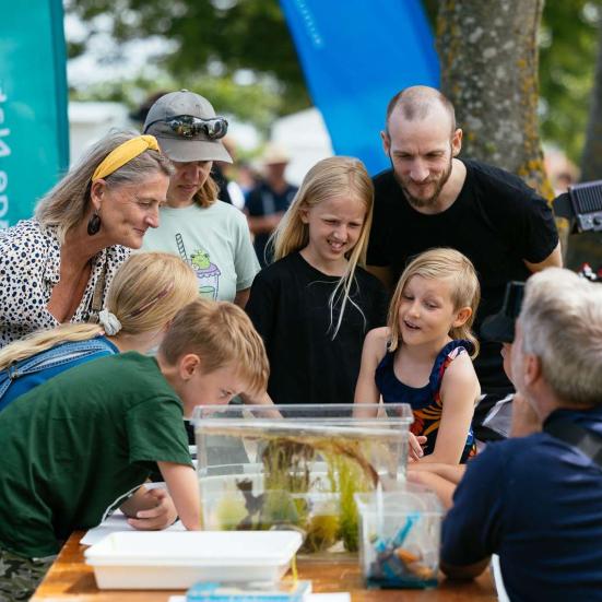Gruppe af bøde børn og voksne som står omkring et bord med et akvarie med havdyr. 