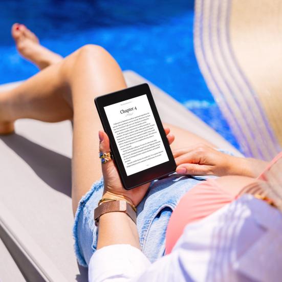 Kvinde på en liggestol i en pool, der læser en e-bog på en e-reader.