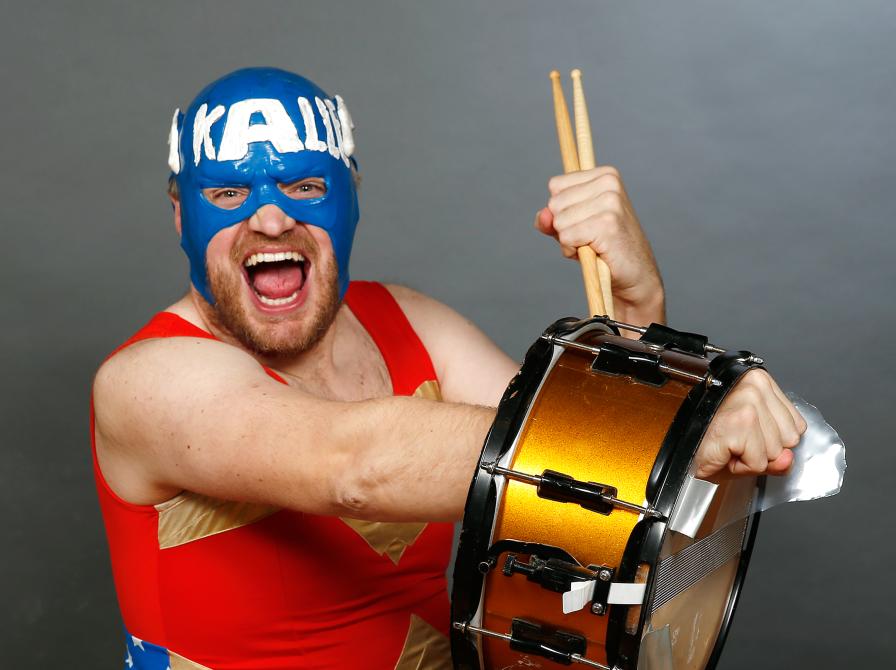 En mand i rød dragt og blå maske spiller trommer og ser vild ud. 