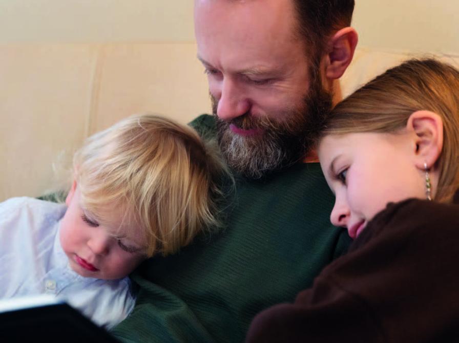 En mand, som læser en bog for to børn, der sidder op ad ham.